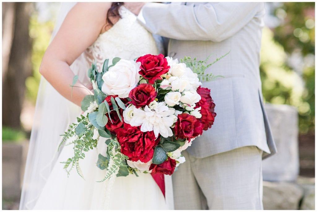 Bride and groom kissing while holding wedding day floral bouquet, white and red flowers.