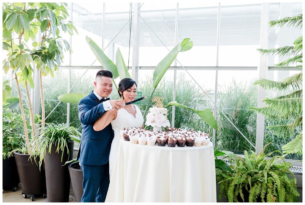 Bride and groom cut cake in greenhouse at Downtown Market.